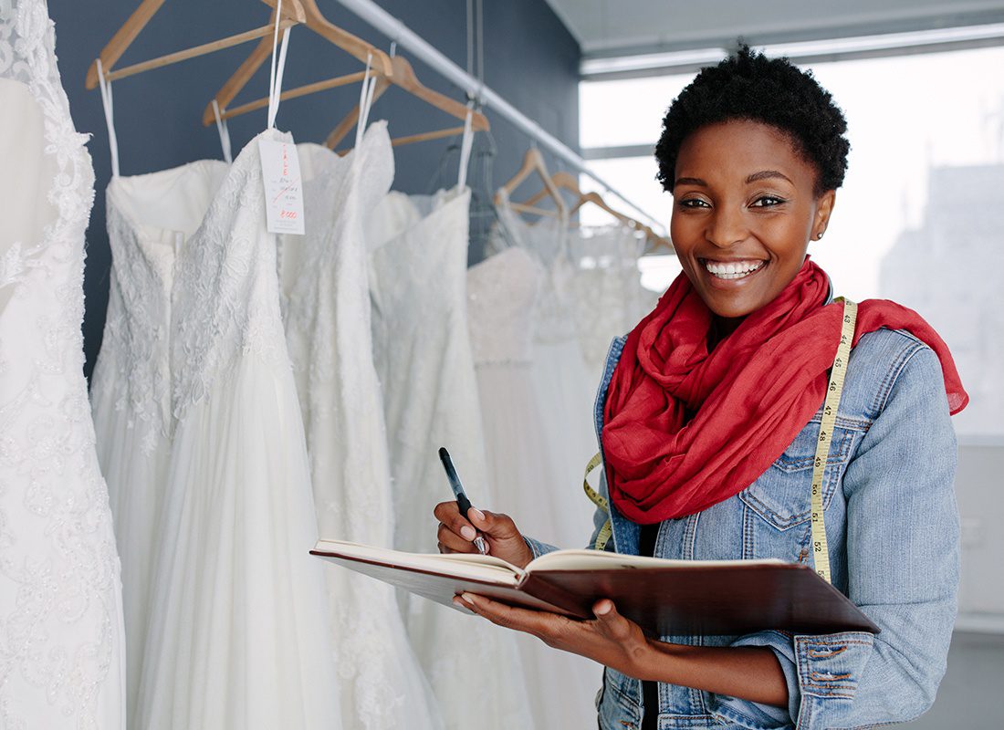 Business Insurance - Friendly Wedding Dress Maker Holds Her Planning Book in Her Shop